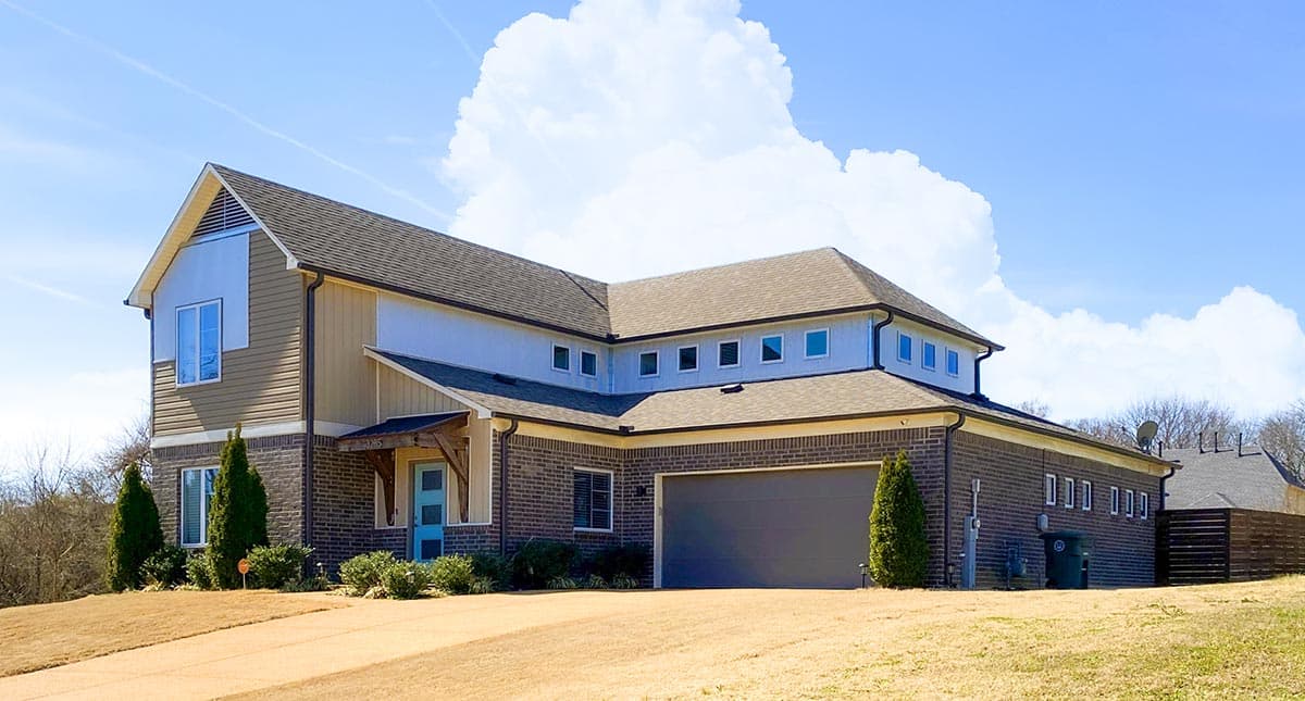 House plan exterior with brick and siding, a prominent gable, multiple rooflines, and a wide garage door.