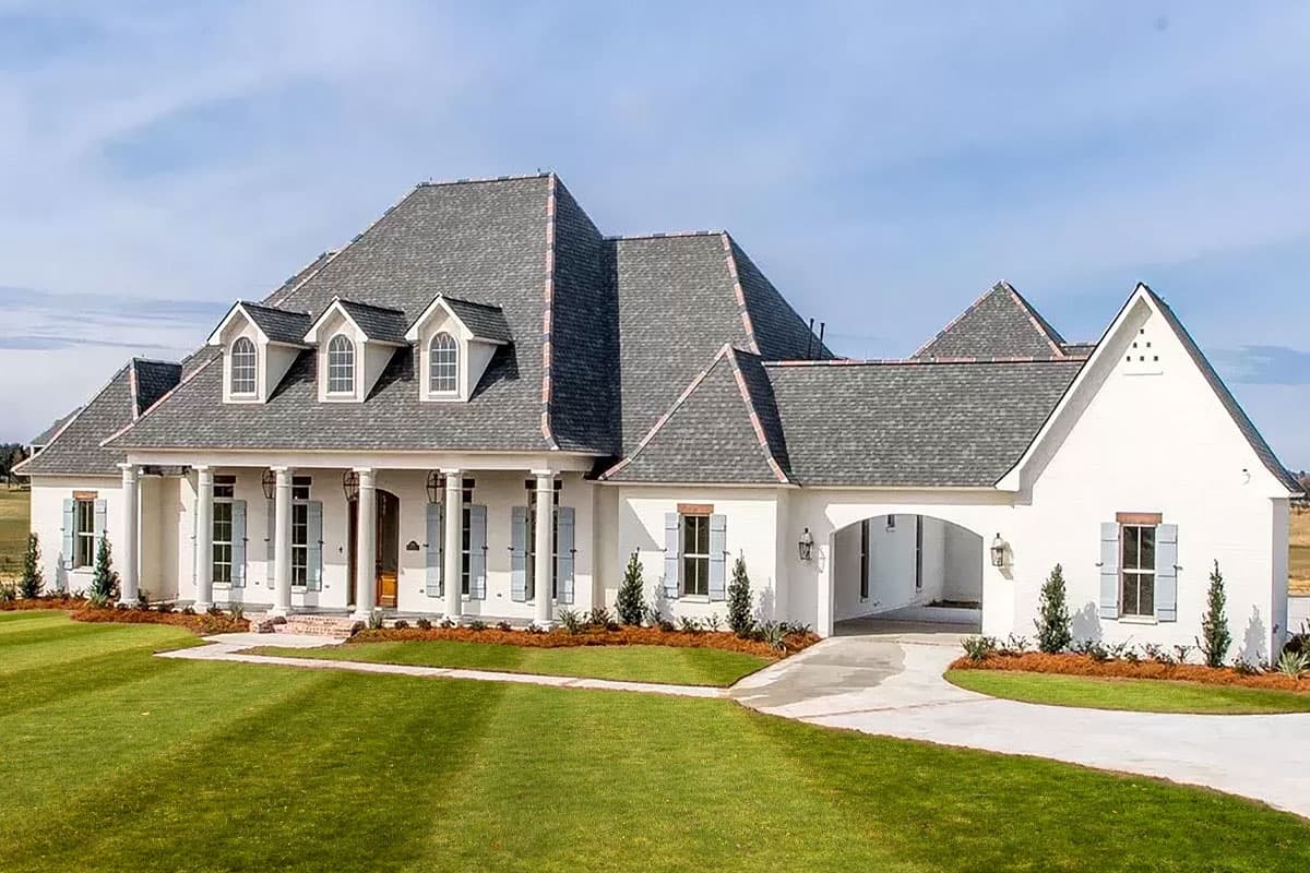 House plan exterior. Two-story French style home with a front porch supported by columns. Features include dormers, gabled rooflines, and a carport.