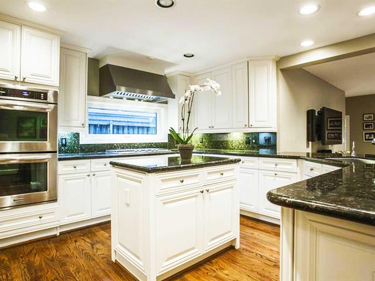 Kitchen with white cabinetry, granite countertops, stainless steel double oven, island, and hardwood floors.