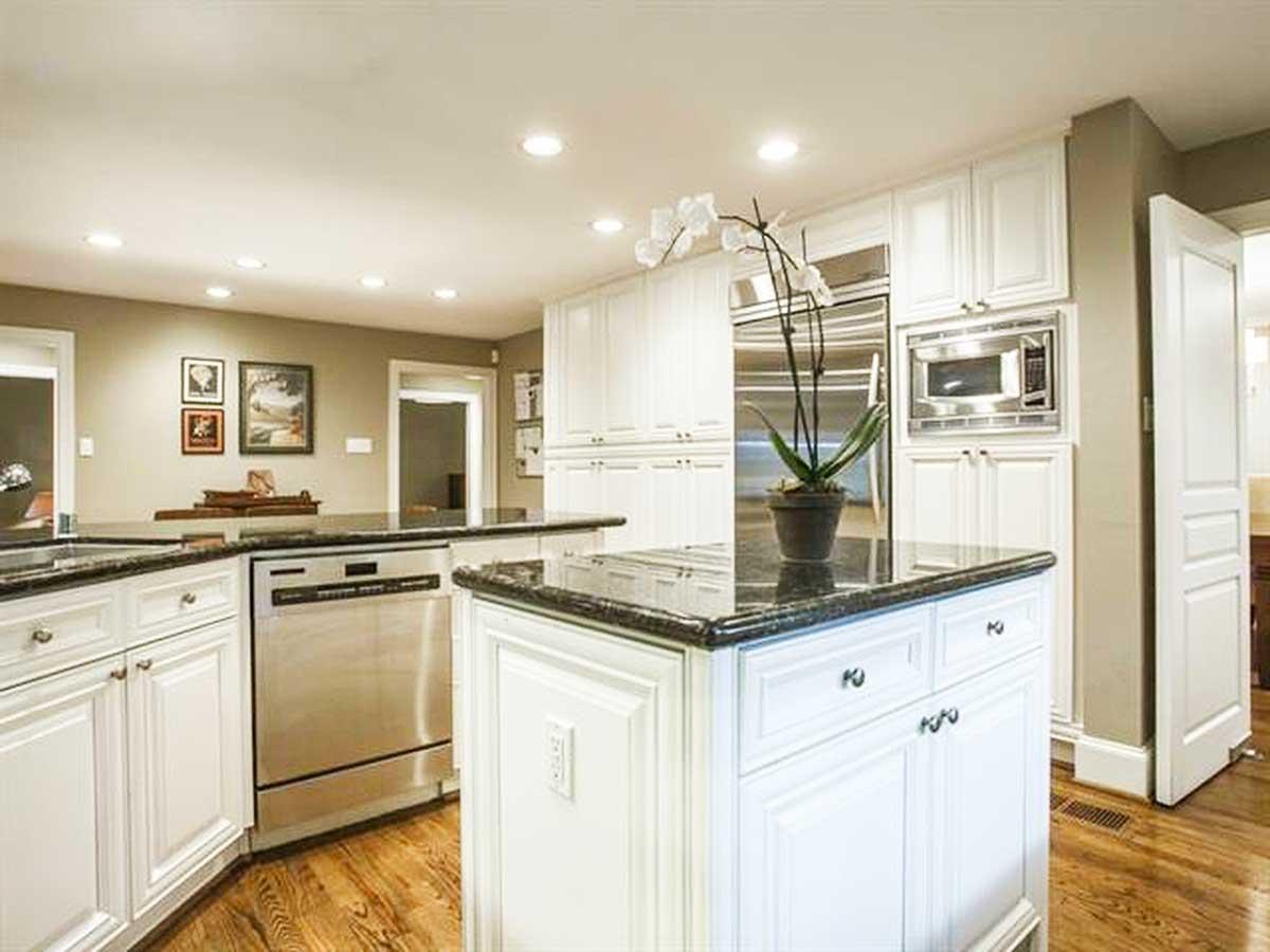 Kitchen with white cabinets, granite countertops, island, stainless steel appliances, and hardwood floors.