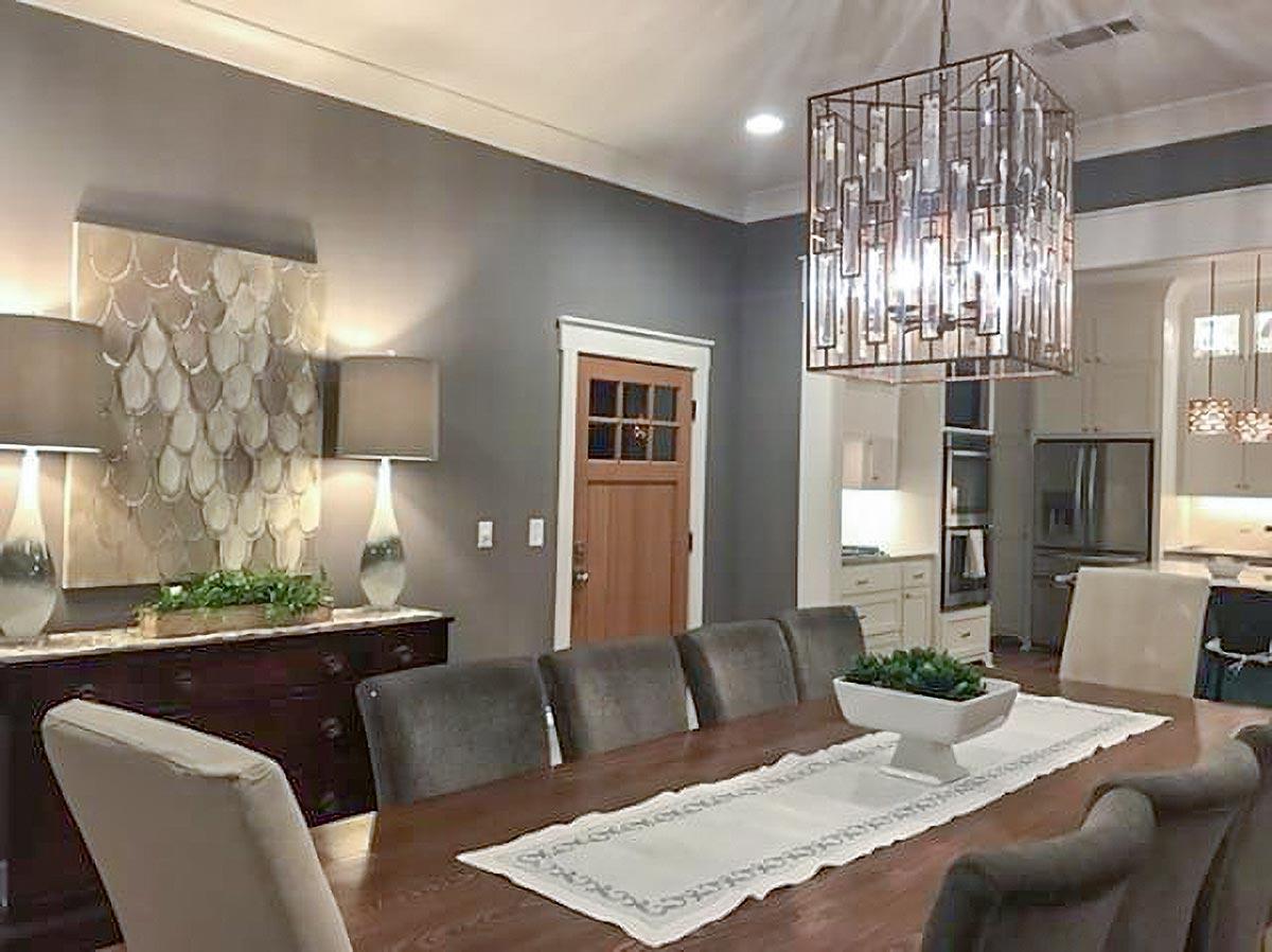 Dining room with a large wooden table, upholstered chairs, a wood-paneled door, and an open kitchen area with cabinetry and appliances.