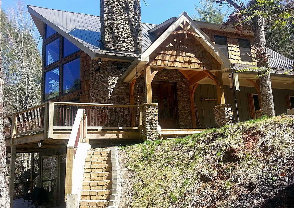 House plan exterior with stone and wood siding, large gabled roofline, prominent stone chimney, and covered porch with timber accents.