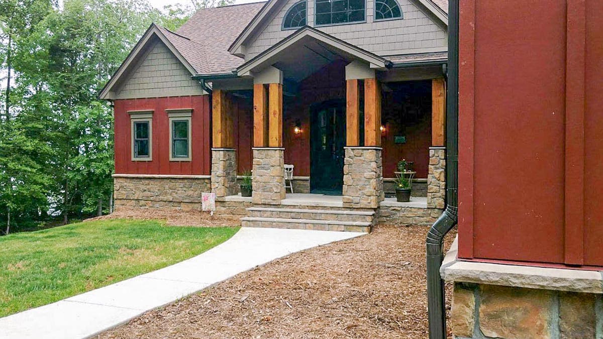 House plan exterior showing stone foundation, wood columns, gable roof, and arched dormer windows.