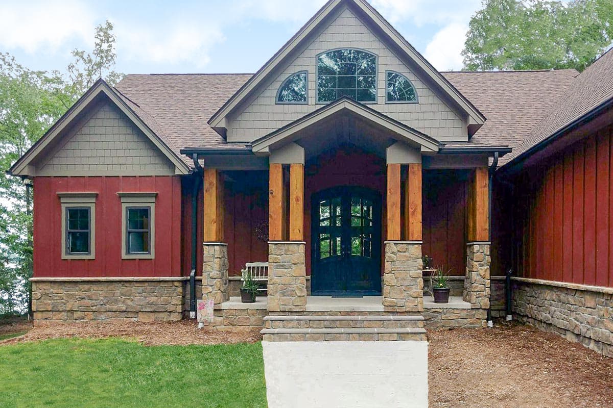 House plan exterior showing a one-story home with a covered front porch, stone accents, timber columns, and arched transom windows above the entrance.