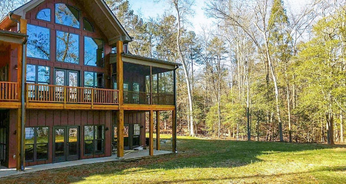 House plan exterior showing a two-story home with a large wall of windows, a screened porch, and a wrap-around deck.