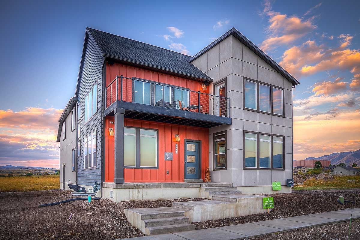 House plan exterior. Modern two-story house with balcony, flat roof, and mixed siding. Features include large windows and a covered entrance.