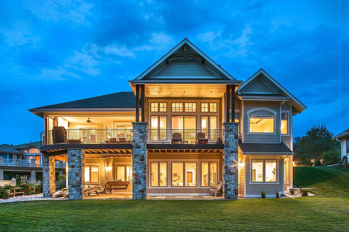 House plan exterior: two-story home with stone accents, upper deck, and lower covered patio with swing.