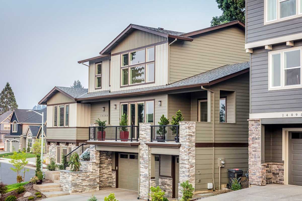 Modern house plan exterior: three stories, gable roofs, stone accents, balconies, and attached garages.