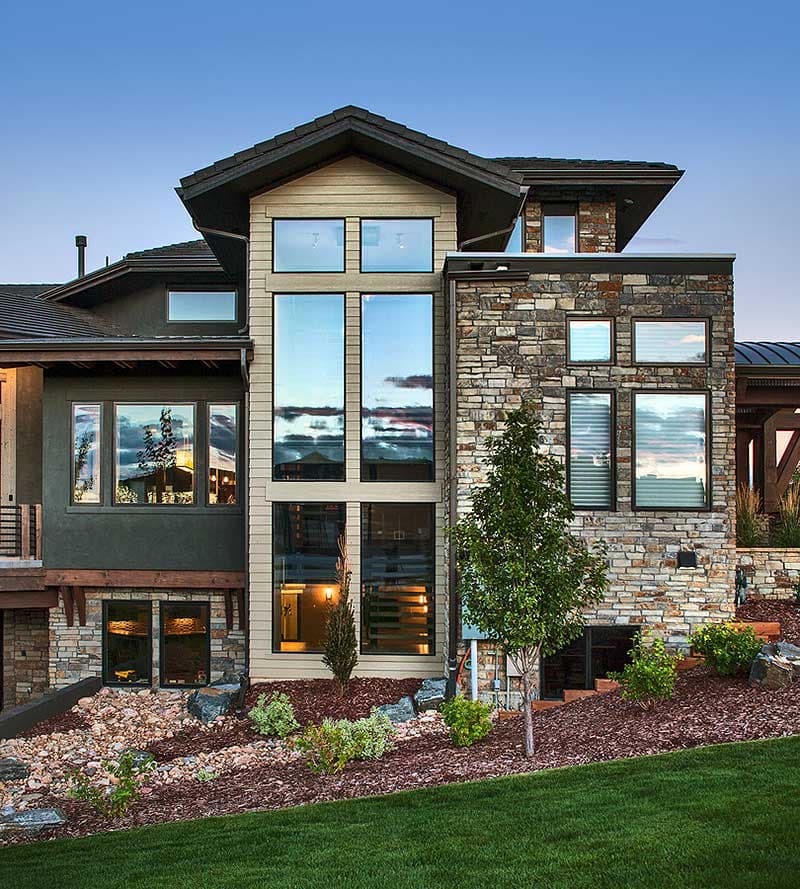 Modern house exterior with stone and stucco, tall vertical windows, and multi-level rooflines.