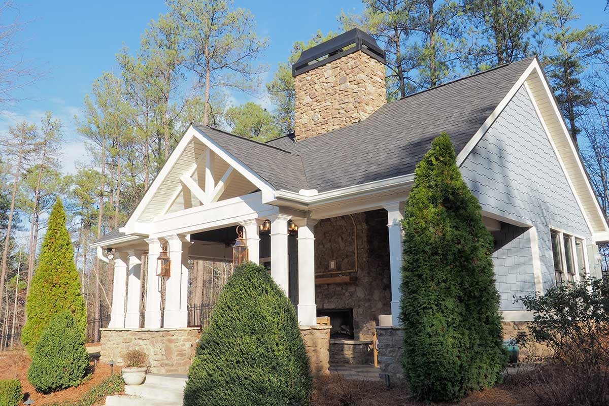 House plan exterior with stone chimney, covered porch with columns, and gabled roofline. Features include cedar shake siding and stone accents.