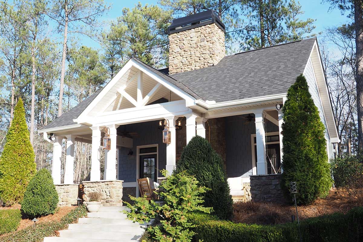 House plan exterior: One-story home with stone accents, a covered porch with decorative trusses, and a prominent stone chimney.