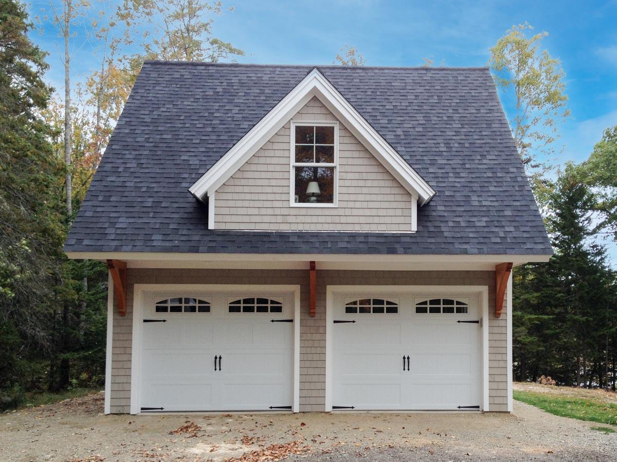 House plan exterior with gambrel roof, two garage bays with arched windows, shingle siding, and decorative brackets.