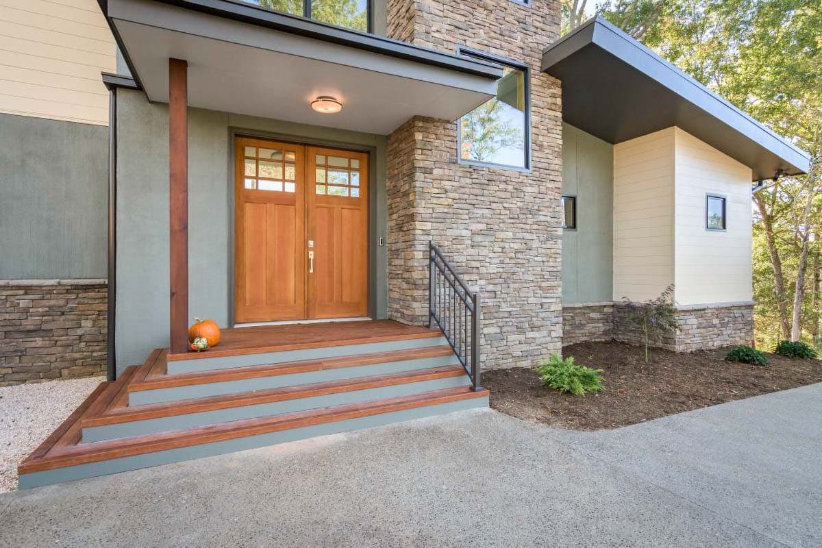 House plan exterior with double wooden doors, stone accents, and a covered entryway with exposed beams.