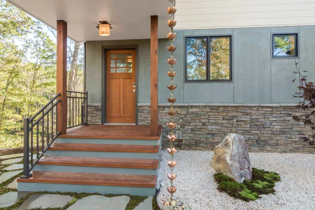 House plan exterior with wooden front door, covered porch, stone and stucco siding, and metal railing.