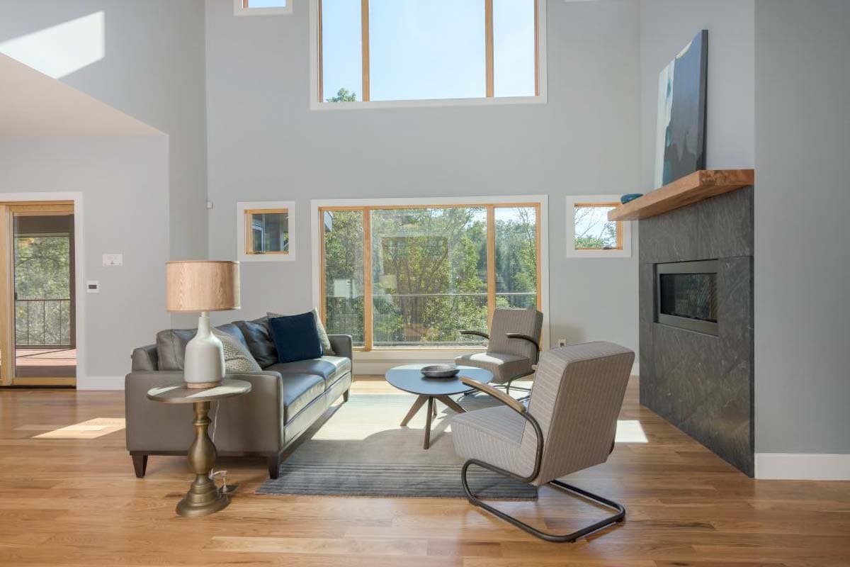 Great room interior with vaulted ceiling, large windows, and a stone fireplace with a modern aesthetic.