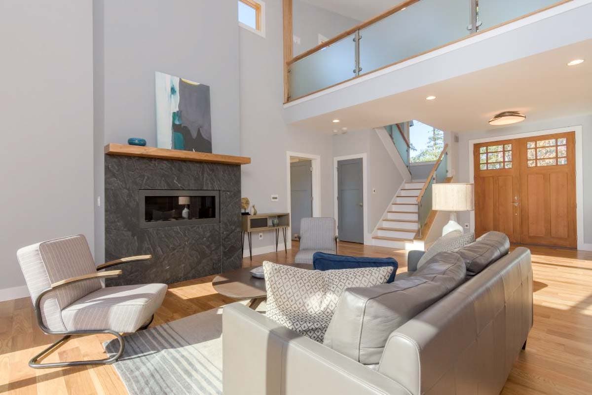 Interior rendering of a great room with a modern fireplace, vaulted ceiling, open staircase, and double entry doors.