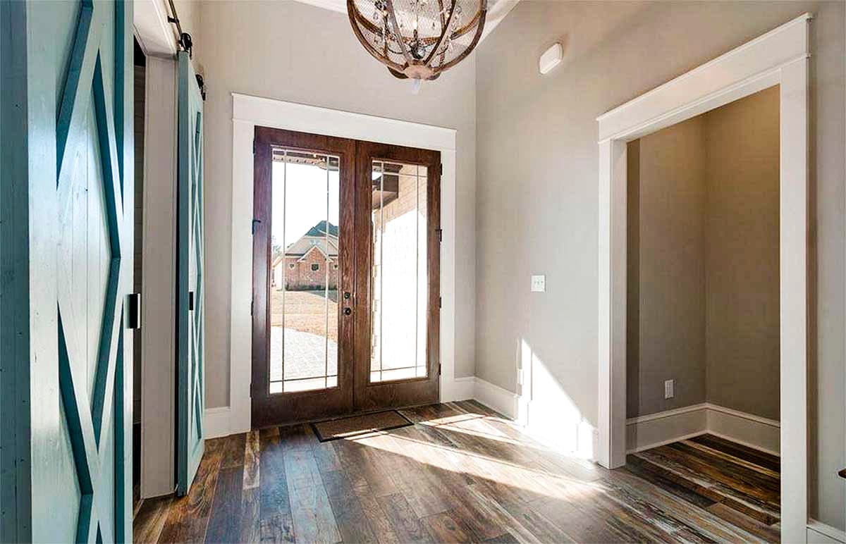 Interior view of foyer with double barn doors, glass-paned double entry doors, and wood plank flooring.
