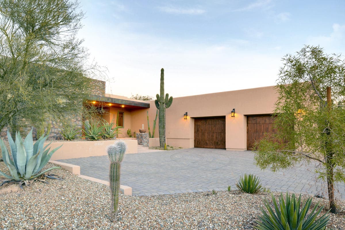 House plan exterior with a stucco finish, stone accents, a covered entry, and a three-car garage with arched wooden doors.