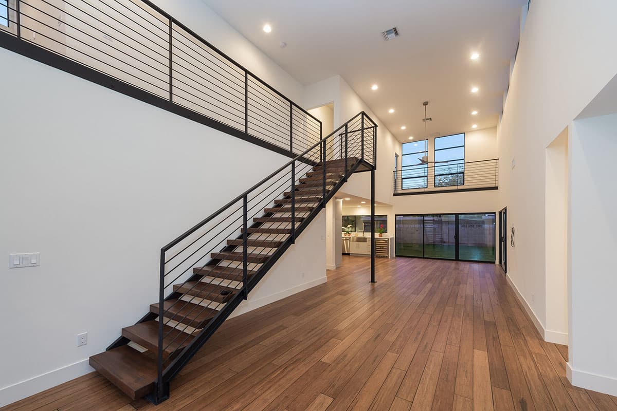 Modern interior with floating wood stairs, open great room, and high ceilings with large windows.