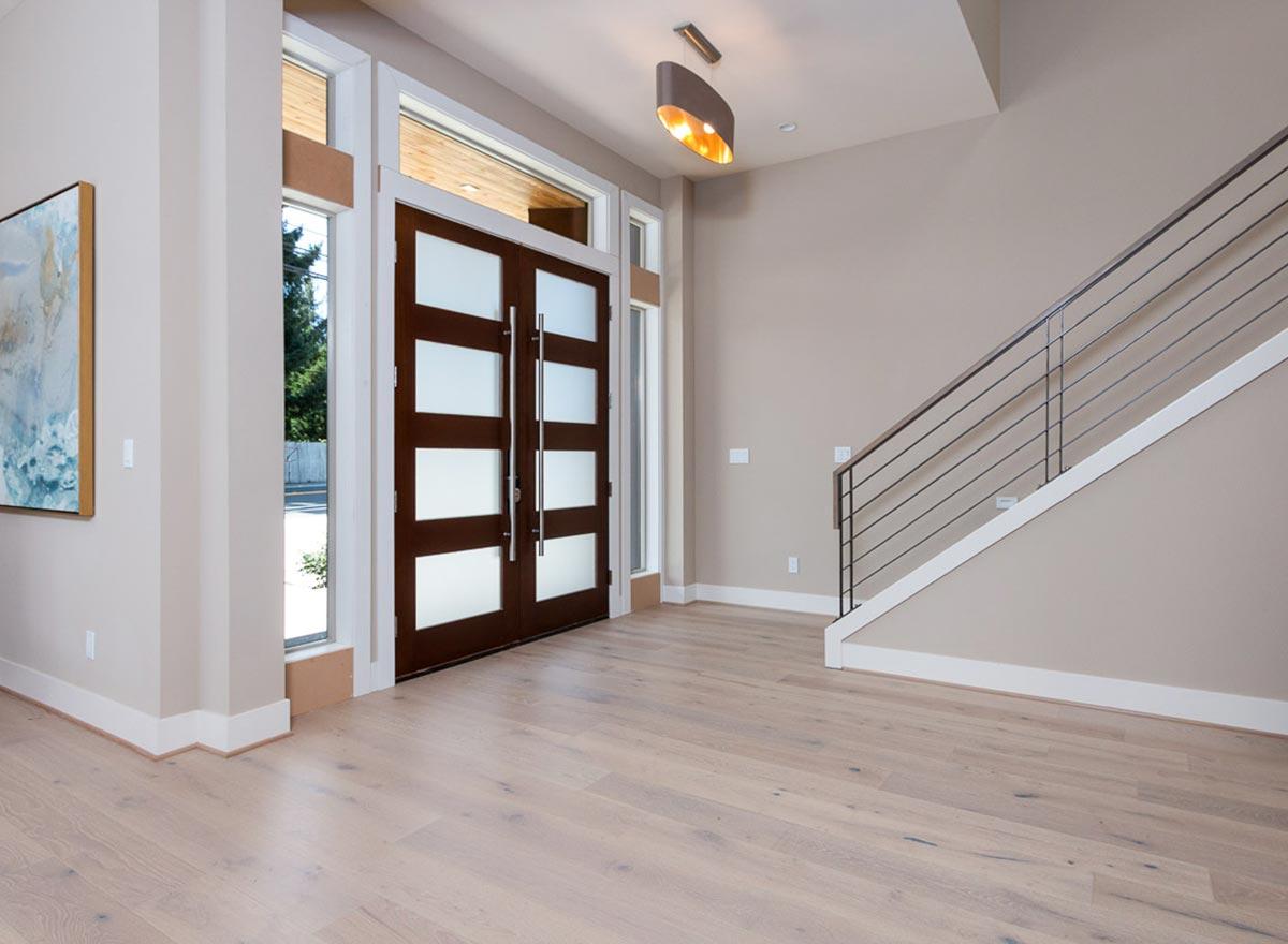 Interior view of a modern entryway with double wooden doors, frosted glass panels, and a metal-railed staircase.