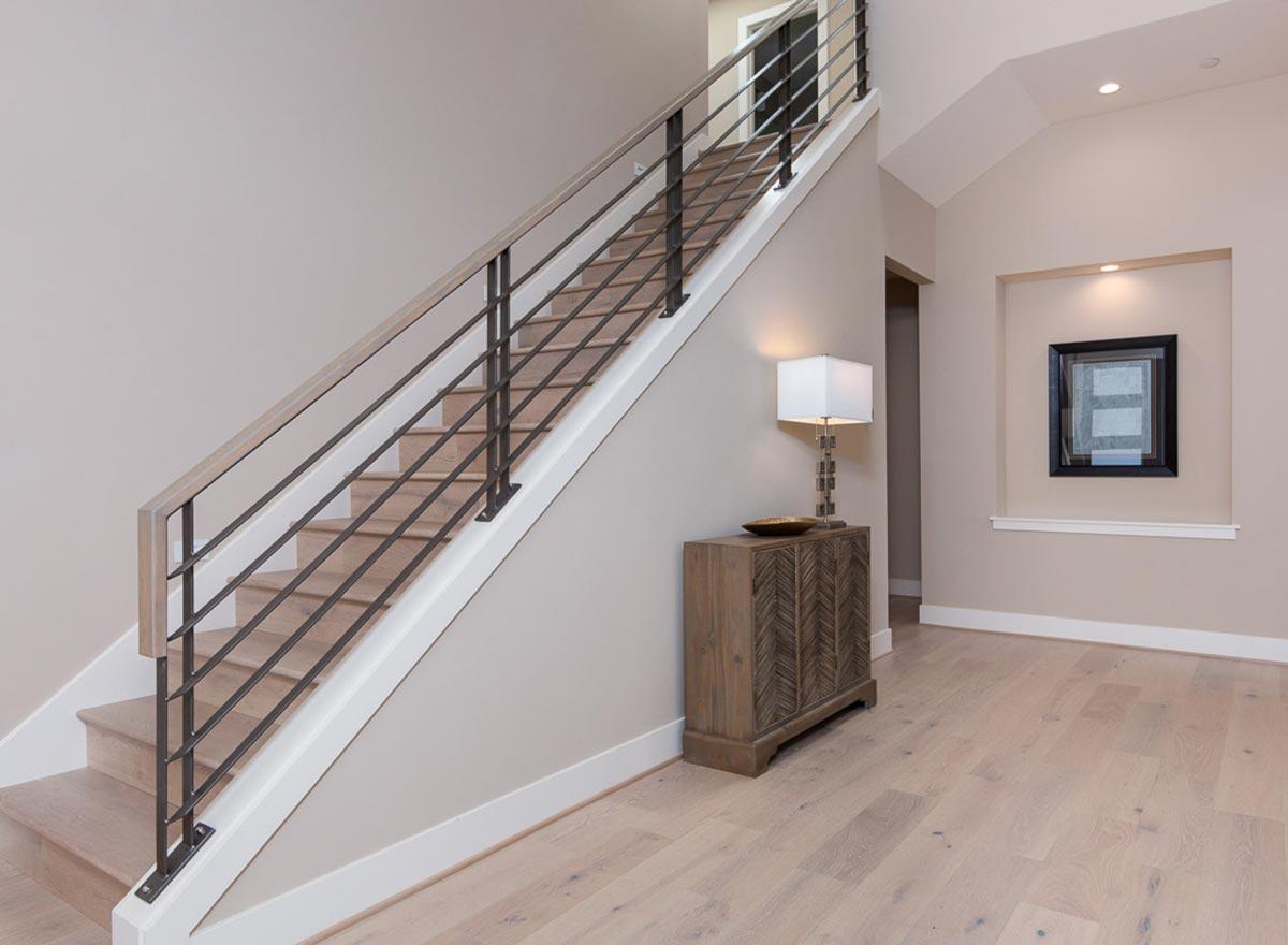 Interior view showing a modern staircase with wood treads, dark metal railing, and white risers. A console table with a lamp is visible.