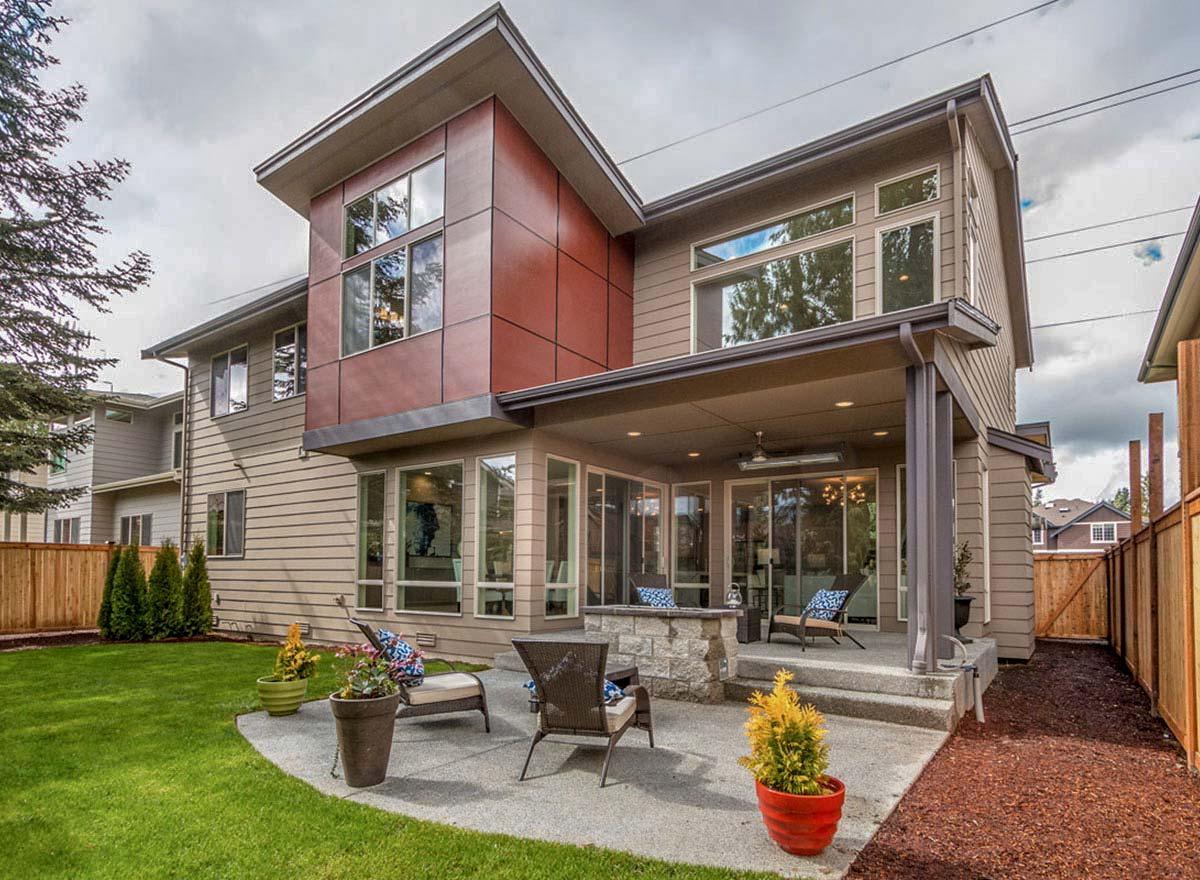 Modern house plan exterior with cantilevered upper level, large windows, covered patio, and stone outdoor fireplace.