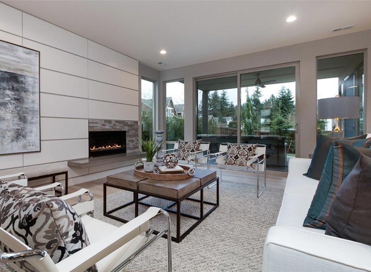 Living room with modern gas fireplace, ample windows, and view of trees and houses.