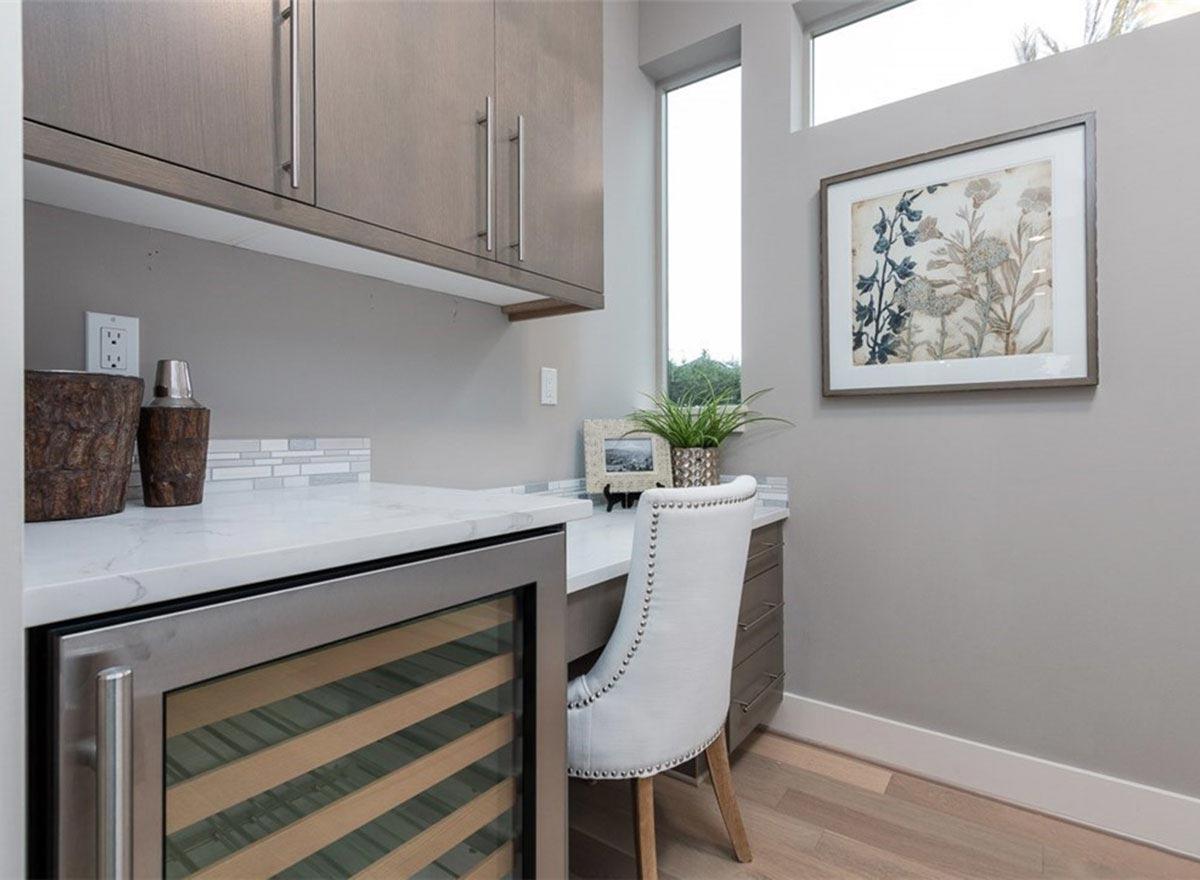 Built-in wine fridge and dry bar with a desk, tufted chair, and elevated windows.