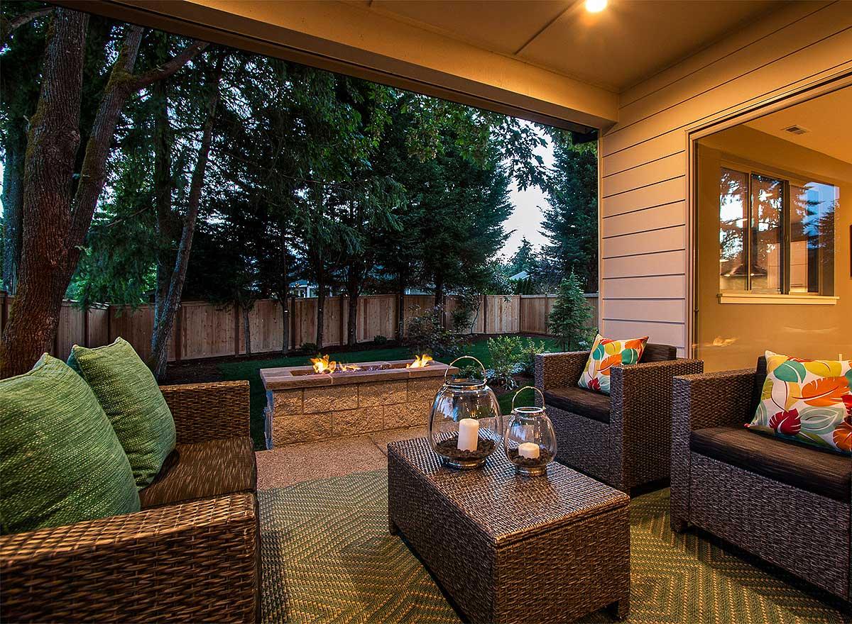 Covered patio with wicker seating, coffee table with lanterns, and gas fire pit.