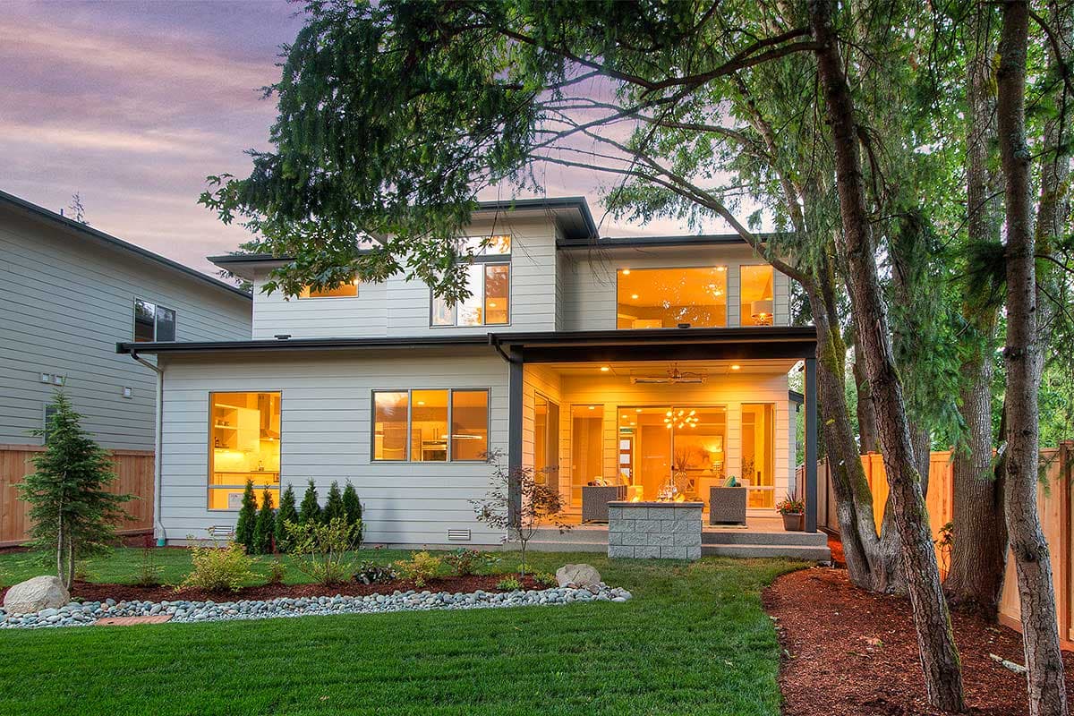 Modern two-story house exterior with large windows, covered patio with fire pit, and sleek siding.
