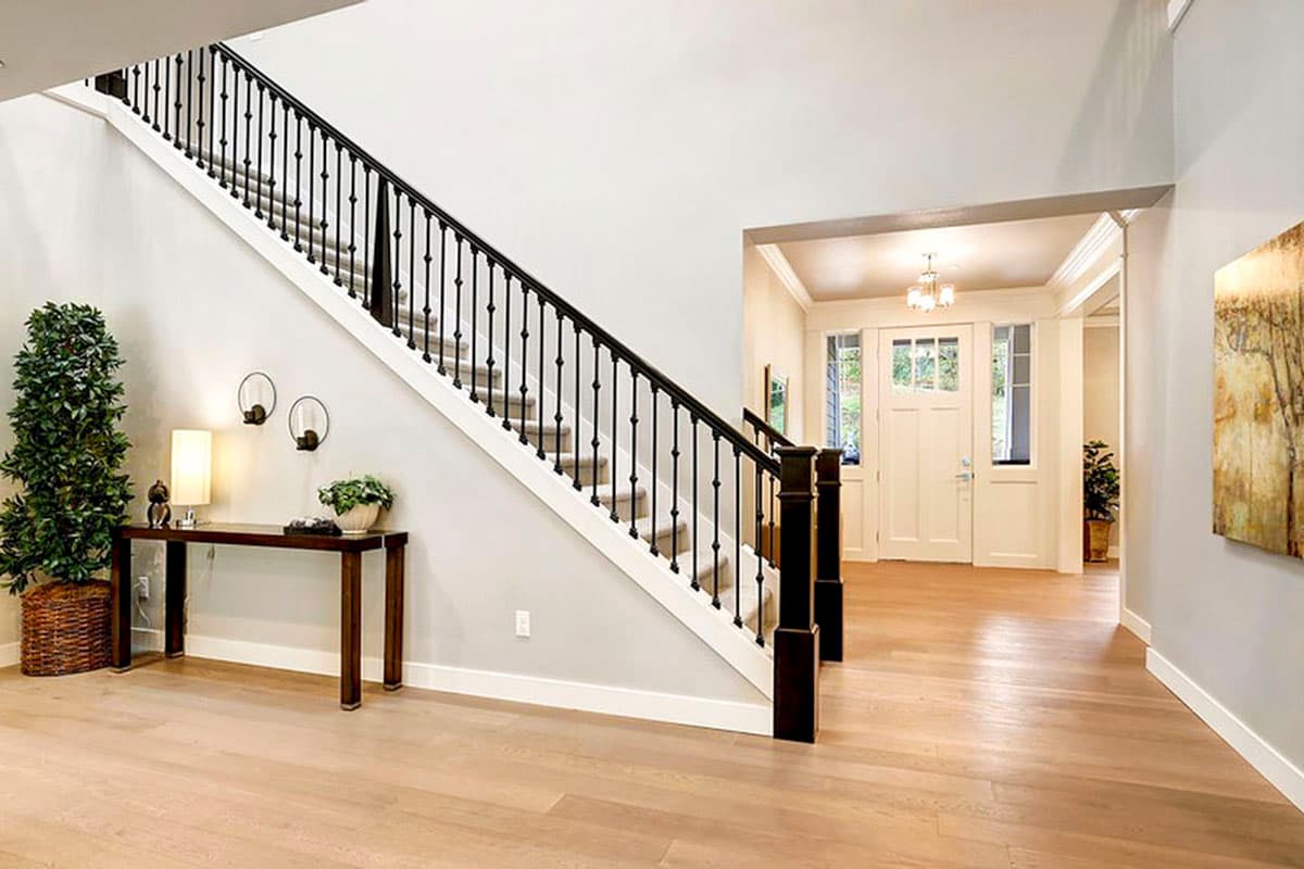 Interior view of a two-story foyer with a grand staircase, light wood flooring, and double front doors.