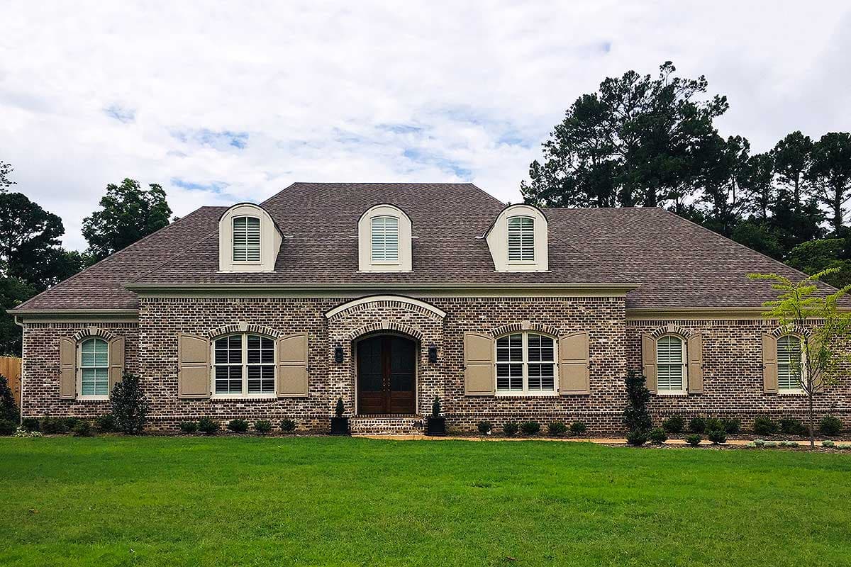 House plan exterior: Brick single-story home with arched entryway, dormers, and louvered shutters.