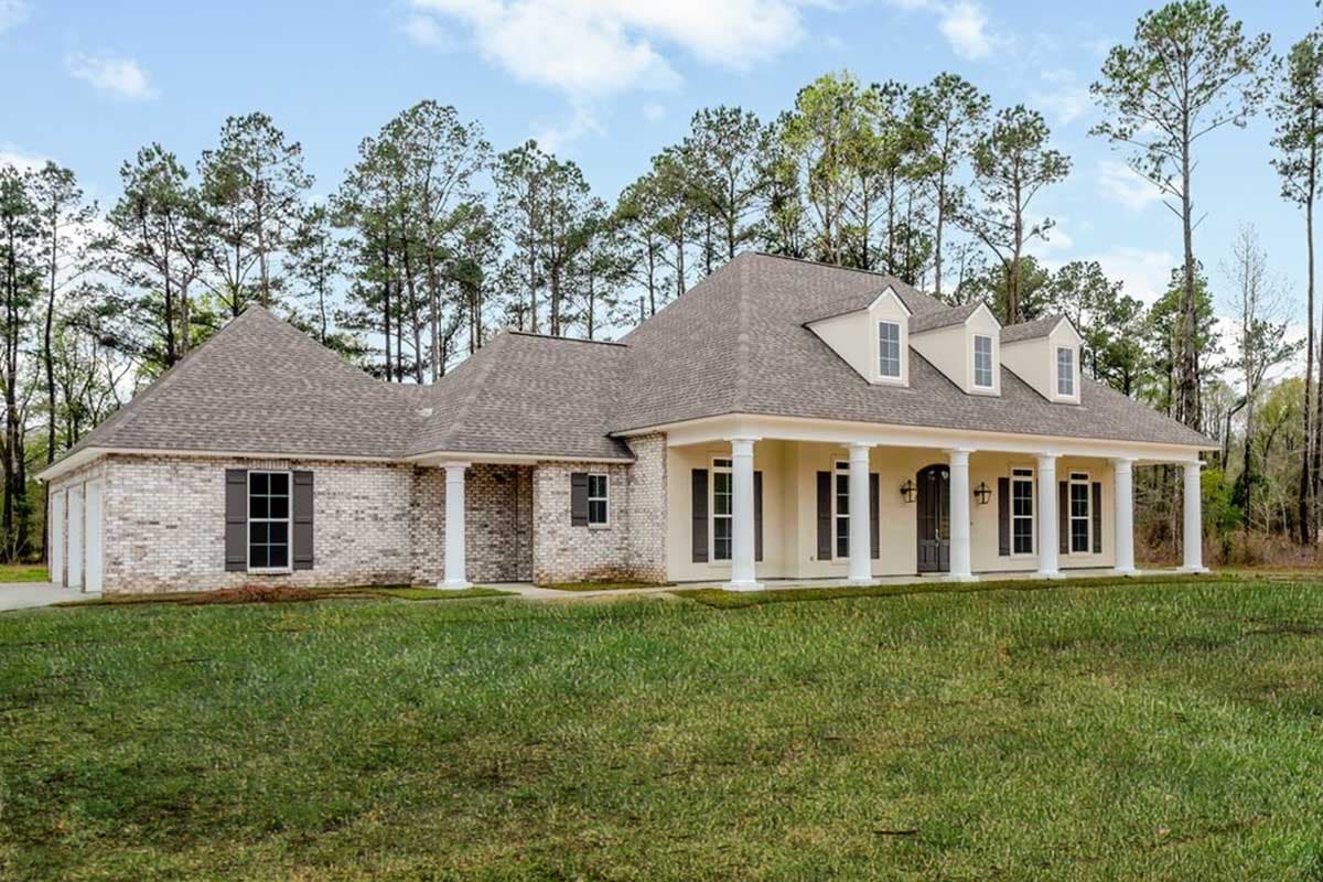 House plan exterior: One-story home with brick facade, wide covered front porch with columns, and multiple gables with dormer windows.