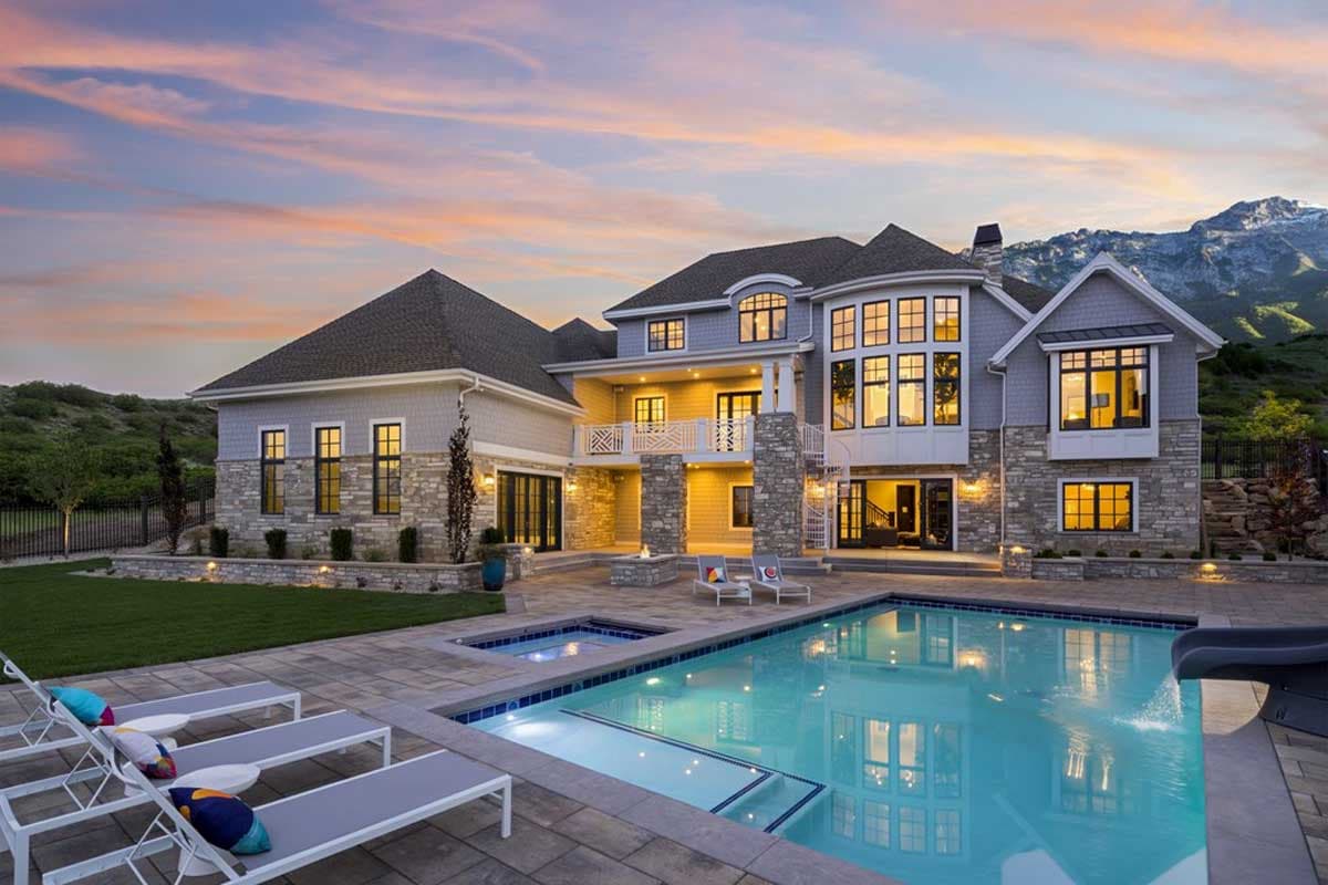 House plan exterior with multiple gables, stone and shingle siding, second-story balcony, and a large swimming pool.