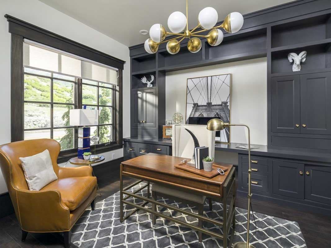 Office with dark gray built-in shelving, a leather armchair, wooden desk, and a large window with a view of hills.