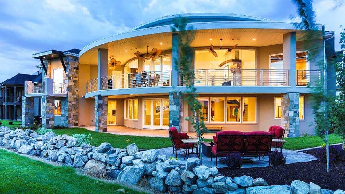 House plan exterior: Modern multi-story home with curved upper level, stone accents, balconies, and extensive windows.