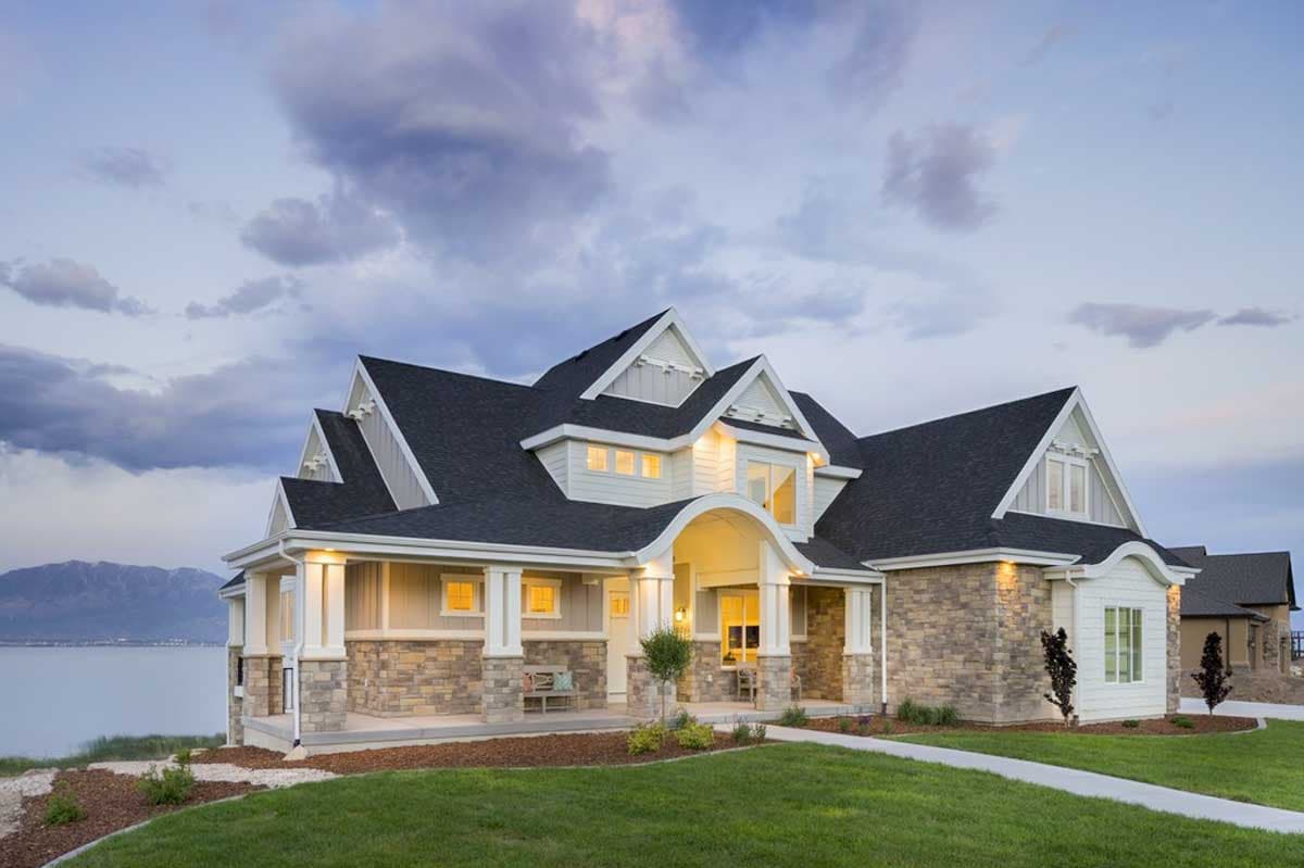 House plan exterior with stone accents, multiple gables, and a front porch. Two-story home with a dark roof and dormers.