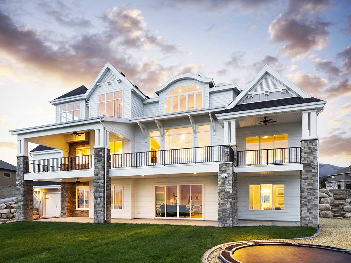 Modern house plan exterior, two stories, featuring layered gables, a covered deck, and stone-clad columns.