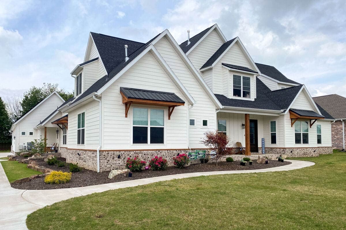House plan exterior. Two-story Modern Farmhouse with gables, dormers, and a covered porch. Features brick veneer foundation and wood brackets.