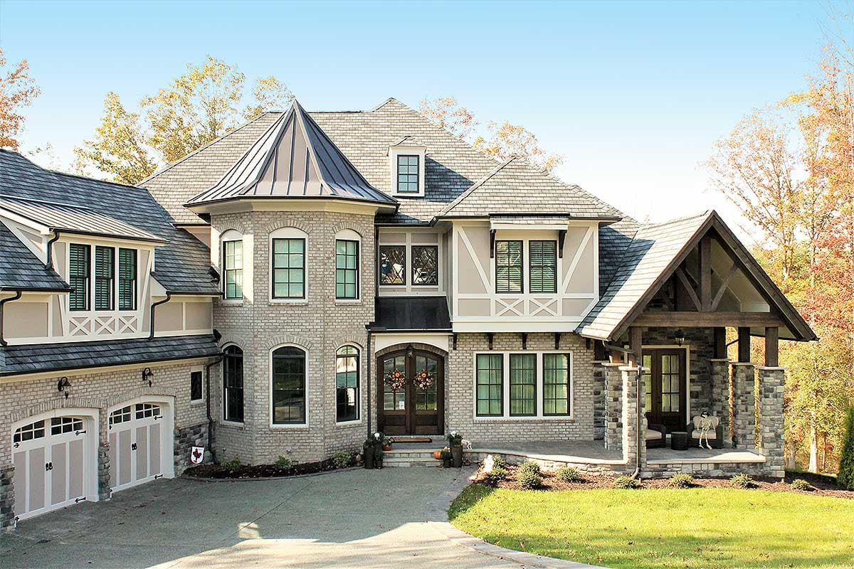 House plan exterior: two-story stone and brick home with a prominent gabled entry, turret, and a side-facing three-car garage.