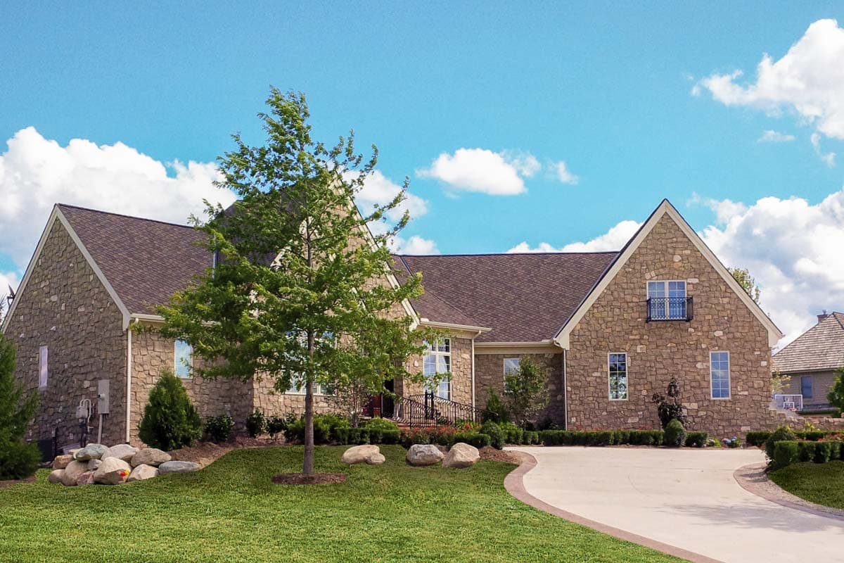 House plan exterior, two stories, stone facade, gabled rooflines, and a Juliet balcony on the upper level.