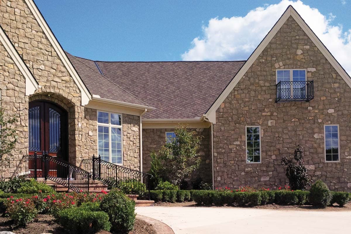 House plan exterior with stone facade, arched entry, multiple gables, and a Juliet balcony.