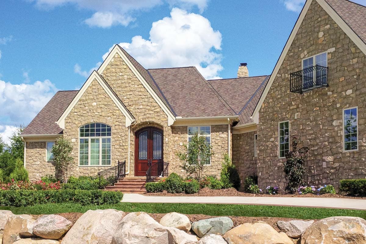 House plan exterior with stone veneer, multiple gables, and a steeply pitched roof. Features include a front entry with arched window and door.