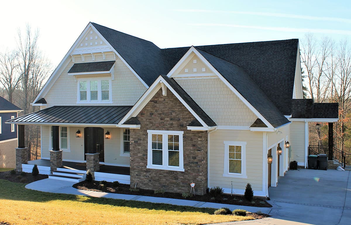House plan exterior: Two-story home with gabled roof, stone accents, covered porch with square columns, and a three-car garage.