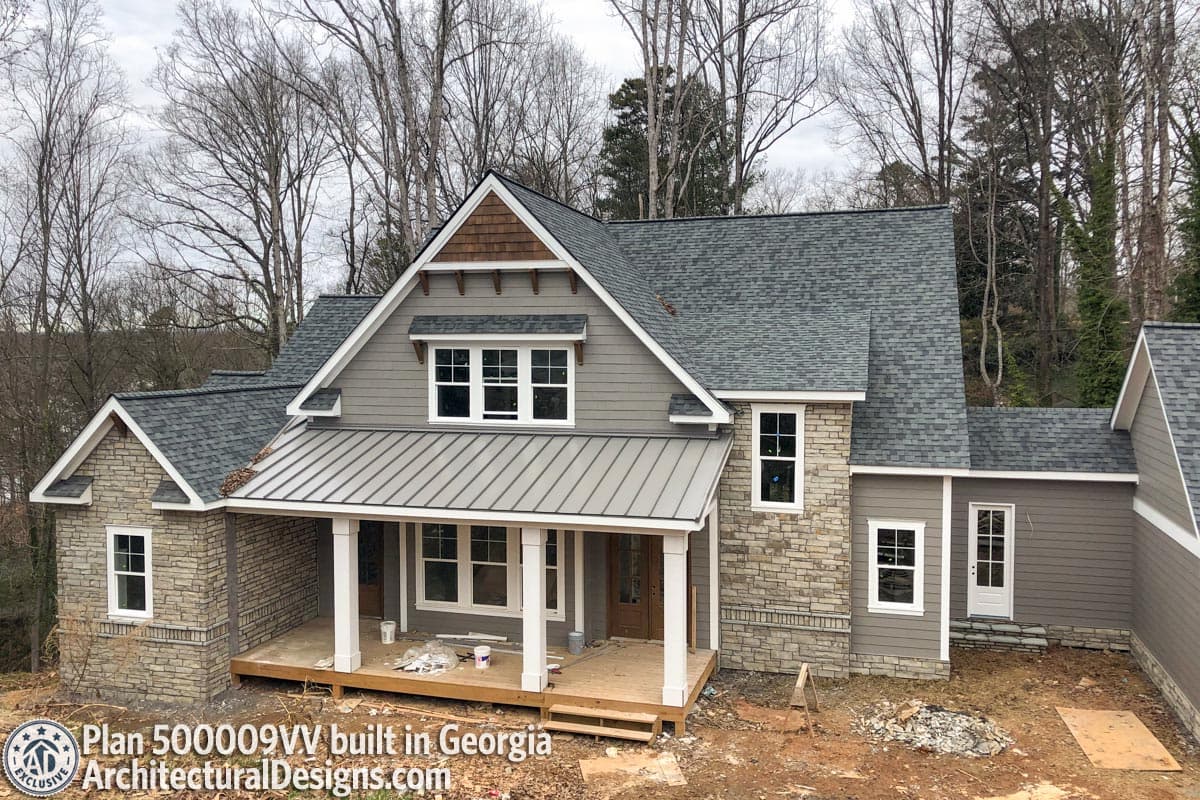 House plan exterior: two-story Craftsman style with stone accents, metal gable roof over porch, and dormer windows.