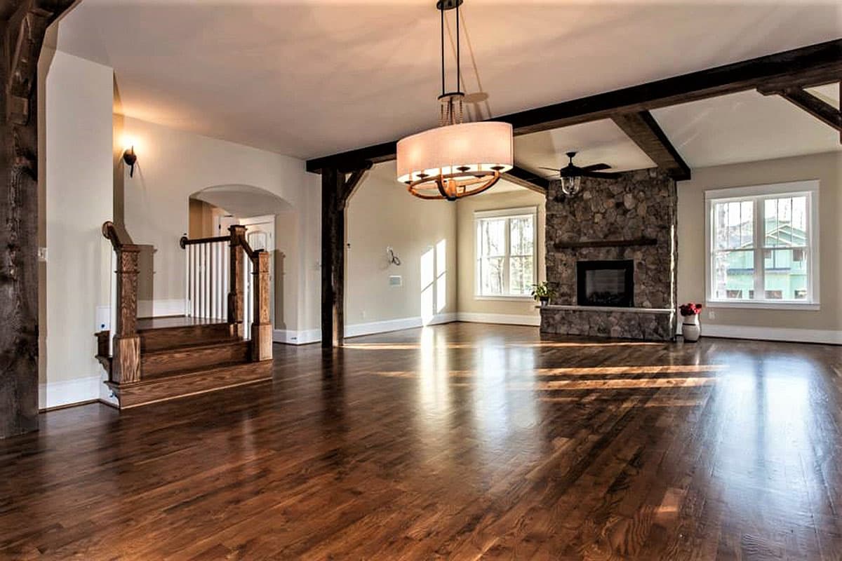 Interior view of great room with stone fireplace, vaulted ceiling with exposed beams, hardwood floors, and staircase.