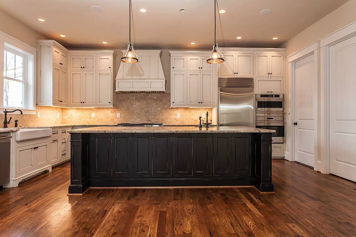 Kitchen with a dark island, white perimeter cabinets, stainless steel appliances, and a farmhouse sink.