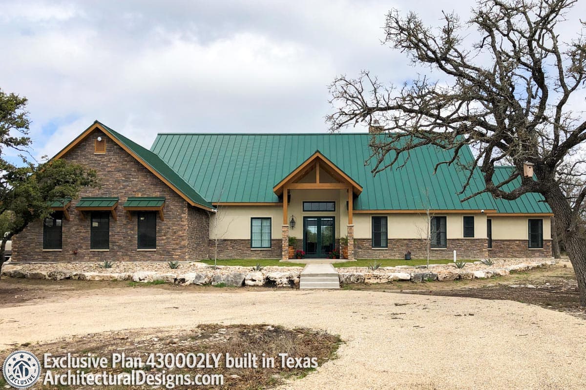 House plan exterior: Single-story Modern style with green metal roof, stone accents, and covered entryway.