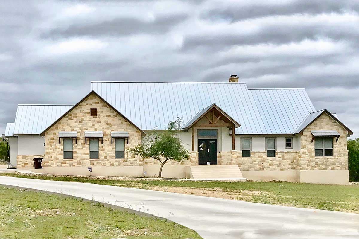 House plan exterior with stone veneer, metal roof, and gabled rooflines. Features an entryway portico and several windows with awnings.