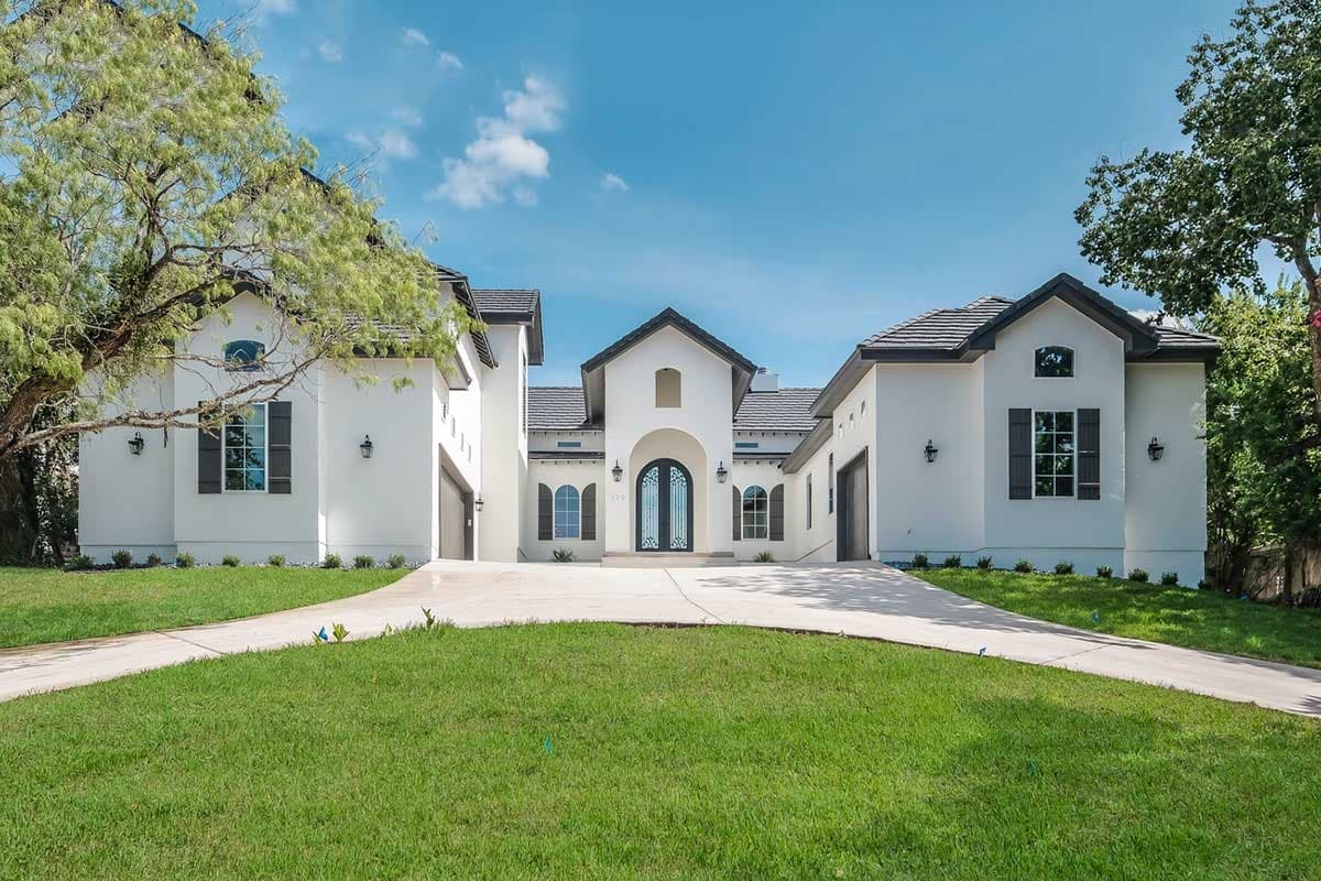 House plan exterior: two-story white stucco home with a central gable, arched double doors, and attached garages.